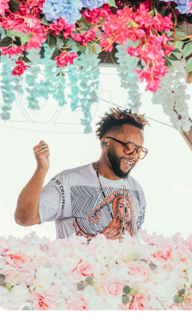 DJ performing behind a bed of white roses under bougainvillea