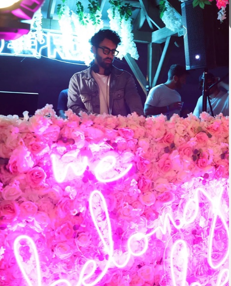 Pink neon sign on a wall of roses at We Belong Here festival